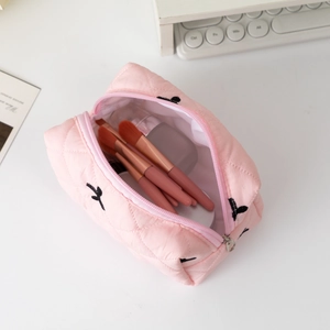 Pink quilted fabric cosmetic bag with bow embroidery and makeup brushes inside