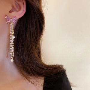 Detail of elegant butterfly earrings with long pearl tassels worn by a model
