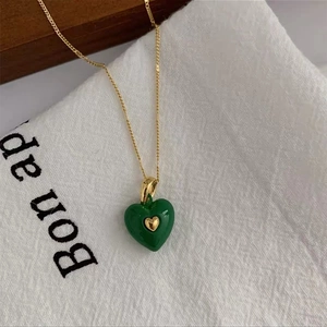 Detailed macro view of a green enamel heart pendant on a delicate gold link chain