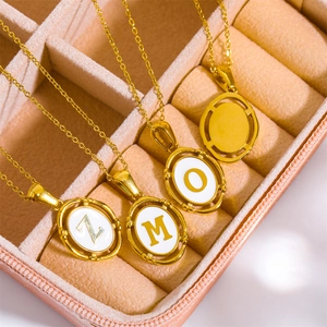 Detail of four golden initial necklaces with white enamel oval pendants in a pink jewelry box