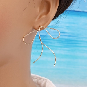 French minimalist gold bow wire earrings with long tassels on a model at sea
