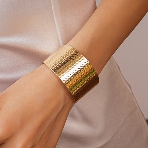 Detail of wide hammered gold cuff bracelet with textured metallic surface on wrist
