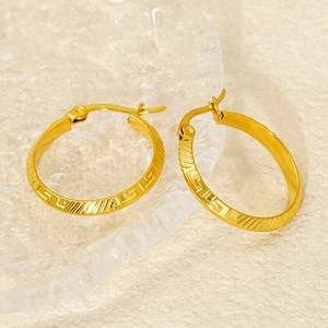 Close-up of gold hoop earrings with Greek key pattern on a glass plate