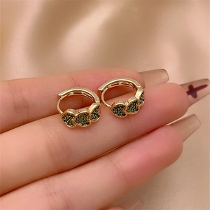 Macro detail of gold hoop earrings with micro-paved green zircon hearts on satin