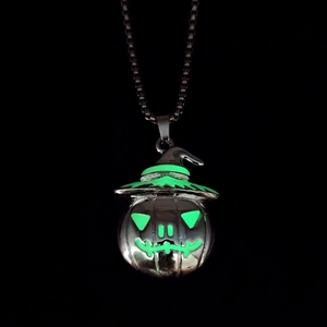Macro shot of Halloween pumpkin witch pendant glowing green in dark background