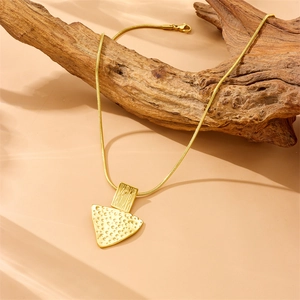 Detailed view of gold triangular pendant with hammered texture hanging on wood