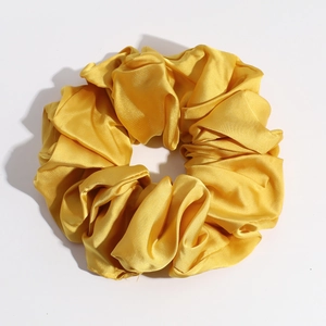 Detail of a large golden satin scrunchie showing glossy silk texture and pleated fabric folds