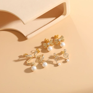 Detail of three pairs of gold earrings with pearls and zircons on a beige background