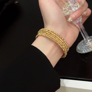 Detail view of a gold plated multi-layer beaded bracelet worn while holding a crystal glass