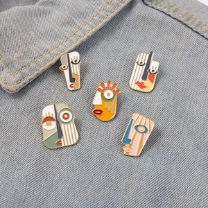 Detail of five colorful Picasso-style enamel face pins on blue denim fabric