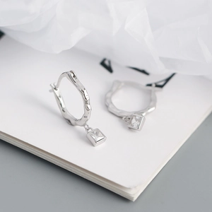 Close-up of irregular silver hoop earrings featuring square cubic zirconia drops