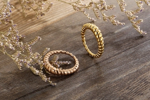 Macro shot of gold and rose gold croissant rings on a textured wooden background