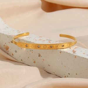 Macro shot of gold star-embossed open bangle with zircon on white terrazzo and beige silk