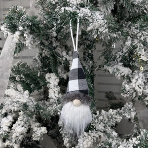 Christmas gnome ornament with black and white plaid hat hanging on snowy pine tree