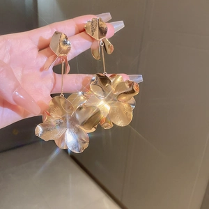 Detailed close-up of large golden floral earrings with brushed metallic texture and starburst glow