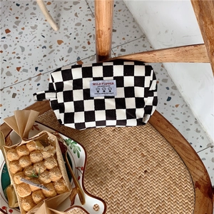 Détail d'une trousse à maquillage en velours côtelé damier avec écusson fleuri