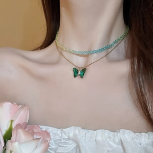 Detail of layered beaded necklace with butterfly pendant on model wearing white top