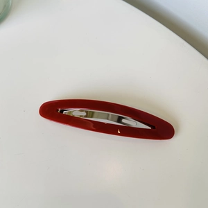 Detailed close-up of a premium red oval hair clip with silver metal base on white background