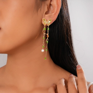 Detail of butterfly tassel earring with gold chain, green crystals and a white pearl