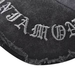 Detailed macro of white gothic embroidery on distressed black washed denim baseball cap