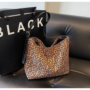 Leopard print tote bag with black strap displayed on a stylish black leather sofa