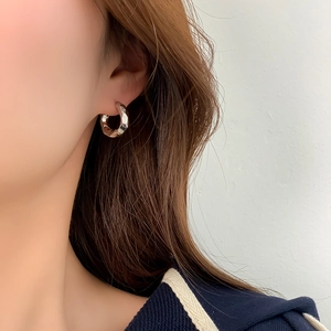 Close-up of silver geometric hoop earrings with reflective facets on a model's ear
