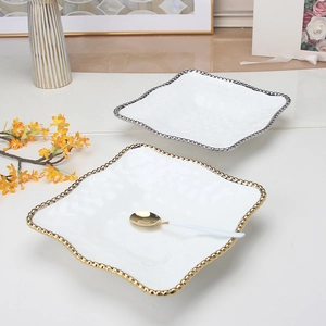 Close-up of elegant square ceramic plates with gold and silver beaded edges and matching spoon
