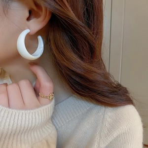 Model wearing a large white resin C-shaped hoop earring with a polished glossy finish