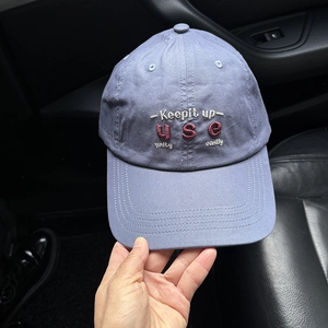 Detail of embroidered letters on a purple washed cotton baseball cap held in hand