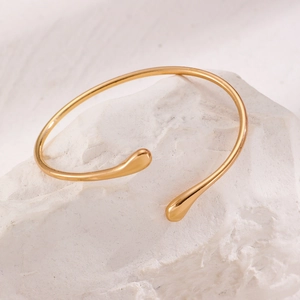 Detailed view of a gold geometric spring cuff bracelet resting on a textured white stone