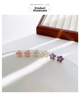 Detail view of dainty floral stud earrings with colorful zircons on a white background