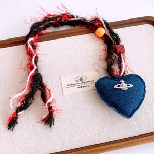 Dettaglio ciondolo cuore in denim con logo saturno argento su cordoncino intrecciato colorato