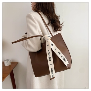 Brown leather tote bag featuring a decorative fashion strap shown on a model