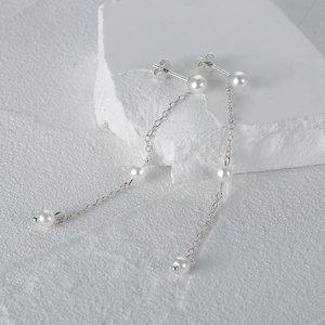 Detail of long s925 silver chain earrings with three pearls on a white stone background