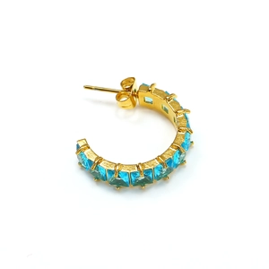 Close-up of golden C-shaped stud earrings featuring light blue square-cut zircons