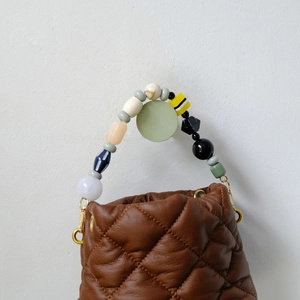 Detail of colorful handmade bead handle on brown quilted handbag with gold hardware
