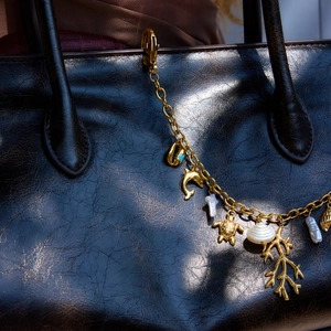 Detail of gold-plated turtle and dolphin charms with pearls on a textured handbag