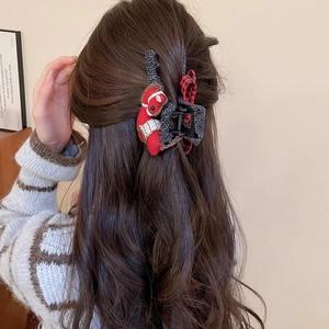 Detail view of large knit hair claw with red plush horse and bow on a textured black base