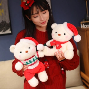 Plush Christmas teddy bear wearing a red hat and sweater held by a person in a cozy home