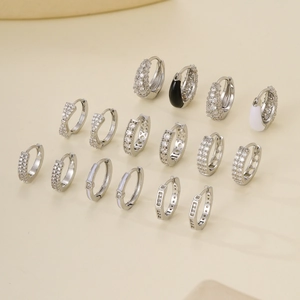 A collection of 16 silver metal hoop earrings with clear zircon stones on beige backdrop