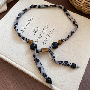Détail du collier en tissu léopard avec perles d'oeil de tigre sur un livre