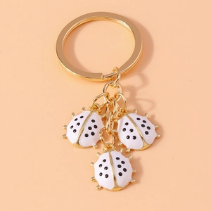 Detail of gold metal keychain featuring three white enamel ladybugs with black spots