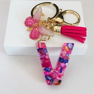 Macro shot of resin letter V keychain with pink stones, gold butterfly and tassel