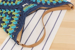 Detail of multi-color woven shoulder bag showing crochet texture and leather strap attachment