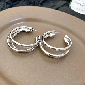 Detail view of silver multi-layer hoop earrings with metallic finish on beige plate