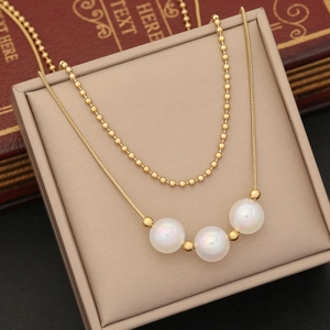 Golden layered necklace with pearls and heart pendant displayed on a beige leather stand