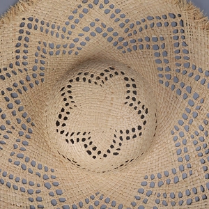 Top view of handwoven raffia sun hat with star pattern cutouts and frayed brim