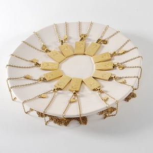 Gold rectangular stainless steel zodiac necklaces displayed on a white ceramic plate