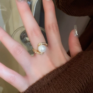 Gros plan d'une bague serpent dorée avec grande perle blanche et zircone sur le doigt