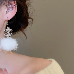 Close-up of model wearing winter acrylic snowflake earrings with white plush pom-pom balls